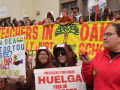 A crowd of adults and children hold a banner saying Keep Teachers in Oakland Schools while other signs say Huelga para un Contracto Justo and Fair Contract Now.