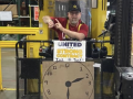 A worker on a forklift points to his watch with a clock sign below him.