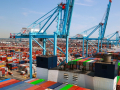 A large ship piled with containers is shown next to a dock with cranes.