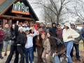 A racially diverse group of 21 workers, including women and men, poses outside in front of the Twin Peaks restaurant. Some have a tough and serious pose while others are smiling widely. Two have arms draped over each other's shoulders and fists in the air. The restaurant facade has a woodsy cabin style, with a logo of two mountains that may be meant to suggest breasts, and the slogan: "Twin Peaks: Eats, Drinks, Scenic Views."