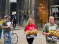 Picketers march outside an office building, most in camouflage shirts. They carry signs: "UMWA ON STRIKE: Unfair Labor Practices"