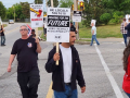 workers walk a circular picket in a driveway, with one visible sign saying “Fighting for our future: Jobs, respect, accountability.”