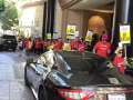 Hotel workers in red t-shirts march past the entrance of a fancy hotel carrying signs that say “Huelga” and “Strike.”.