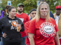 A determined-looking woman with a crowd behind her wears a red shirt saying UAW, Back in the Fight