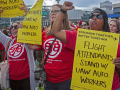 Three women wearing red Association of Flight Attendants shirts hold yellow signs saying, "Flight Attendants Support UAW Auto Workers."