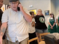 Starbucks workers in aprons surround a manager in a white shirt, the manager is leaving and talking on the phone