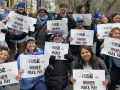 About 15 smiling people hold identical signs saying “ARISE for Higher Para Pay”