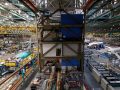 An aircraft factory floor is viewed from above, with planes on either side and high rafters above.