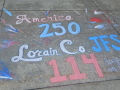 Chalk graffiti on sidewalk says “America 250, Lorain Co. JFS 114 days on strike”