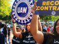 Four Black women march with t-shirts that say “Labor vs. Corporate Greed.” They’re holding UAW signs.