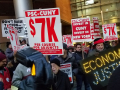 crowd holding signs including "PSC-CUNY $7k per course for adjuncts," "invest in CUNY, invest in New York," and "ECONOMIC JUSTICE" spelled out in lights