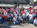 Un grupo de cincuenta trabajadores con gorras rojas y camisas blancas levantan sus puños y posan para la cámara.