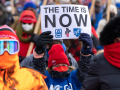 Marchers bundled in coats, one carries printed sign: "The time is now!"