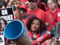 Black woman raising her fist in a crowd of strikers