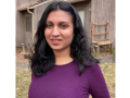 Sindhu poses outside in front of a barn. She has long black hair and is wearing a red shirt and a slight smile.