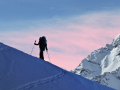 Silhouette of a skier ascending a mountain slope with pink sky in background