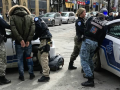 Outdoors, four police officers handcuffing two people against two police cars