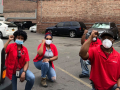 Four Black workers in red Verizon shirts kneel in a parking lot, fists raised.