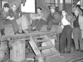A group of autoworkers sit on a makeshift platform under a window in a factory.
