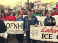 People march in the street carrying various banners and signs. The most visible banners says "Labor says ICE out." Others partially visible are for two Oregon health care unions, OFNHP and ONA. Their red and green shirts (respectively) are also visible, and someone has a blue AFT shirt. Many handmade picket signs are visible, including "We are all Alex," "Unions want ICE out," "Hold ICE accountable," and "Ge(stop)o the bullshit" 