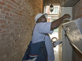 A letter carrier with a big shoulder bag puts mail in a grouped mailbox in an alley, he is backlit.